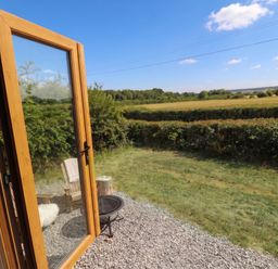 A view from an open door with a chair and table in the garden at Cariad Mawr Gwaenysgor near Prestatyn
