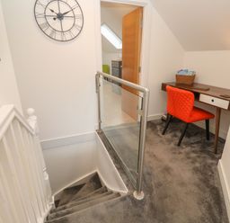 Stairs with grey carpet leading to a small workspace with a wooden desk and red chair at Cuckoo's Rest in Penryn