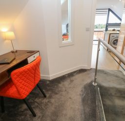 An upstairs hallway with a wooden desk and orange chair next to a lamp and a view into a kitchen with a washing machine at Cuckoo's Rest in Penryn