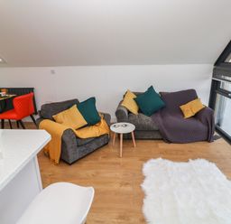 A living room with two gray sofas with colored cushions next to a small white table and a white fluffy rug at Cuckoo's Rest in Penryn