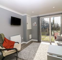 A living room with a wall-mounted television and large sliding glass doors leading outside at Caldwell Cottage in Lanark