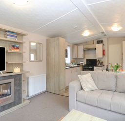 A living room with a gray sofa a fireplace and a television next to an open kitchen at No 3 Foxburrow Hang Belton