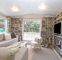 A living room with sofas a small chair a coffee table a television on a wooden shelf and large windows with patterned curtains at No 3 Foxburrow Hang in Belton