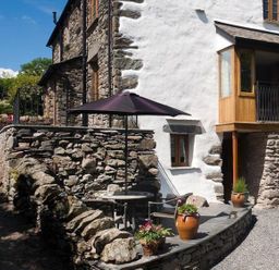 An outdoor seating area with a table umbrella and stone walls at The Cosy Peacock in Troutbeck
