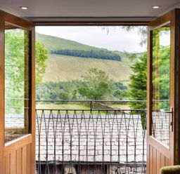 An open wooden double door leading to a small balcony with a metal railing overlooking green hills and trees at The Cosy Peacock in Troutbeck