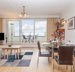 A dining area with a glass table set with glasses and plates next to a living area with a TV and coffee tables near a balcony with outdoor chairs and a table at Mariners Watch in Carbis Bay