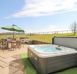 An outdoor patio area with a hot tub wooden table with umbrella chairs and garden seating at Cuckoo Pen Cottage in Eastham near Tenbury Wells