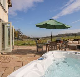 An outdoor patio with a hot tub table with chairs umbrella a barbecue and seating at Cuckoo Pen Cottage in Eastham near Tenbury Wells
