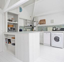 A white kitchen with appliances and shelves at The Net Loft in Mousehole