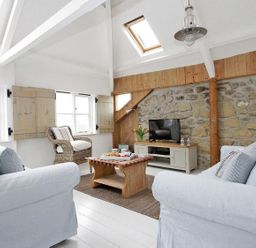 A living room with two white sofas a wooden coffee table a wicker chair a TV on a cabinet and skylights at The Net Loft in Mousehole