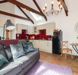 An open plan living room and kitchen with a gray sofa and floral cushions at The Stables Ruthvoes near St Columb Major