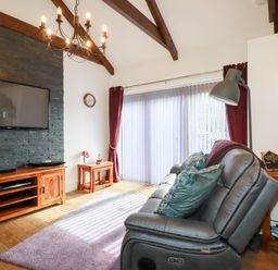A living room with a gray leather sofa pillows and lamp next to a wooden TV cabinet and stone wall at The Stables in Ruthvoes near St Columb Major