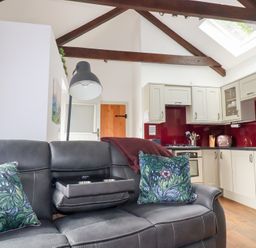 A living room and kitchen area with a gray sofa and floral cushions at The Stables in Ruthvoes near St Columb Major