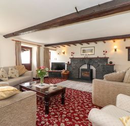 A living room with sofas a wooden coffee table a stone fireplace and a television at Addyfield Farmhouse in Cartmel Fell near Bowland Bridge