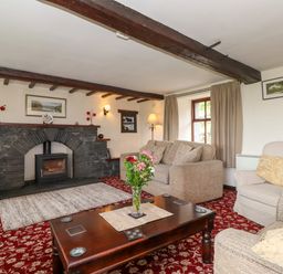 A living room with a stone fireplace wooden beams and sofas at Addyfield Farmhouse Cartmel Fell near Bowland Bridge