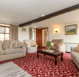 A sitting room with sofas and armchairs around a wooden coffee table on a patterned red carpet at Addyfield Farmhouse in Cartmel Fell near Bowland Bridge