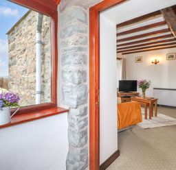 A living room with a television flowers on a table and wooden beams on the ceiling at Addylea Cottage in Cartmel Fell near Windermere