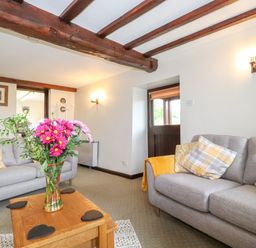 A living room with two gray sofas a wooden coffee table with flowers and exposed wooden beams on the ceiling at Addylea Cottage in Cartmel Fell near Windermere