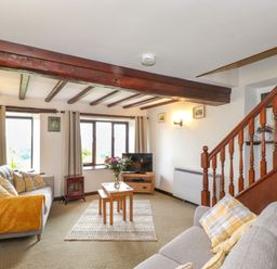 A living room with two sofas wooden beams wooden staircase and a television at Addylea Cottage in Cartmel Fell near Windermere