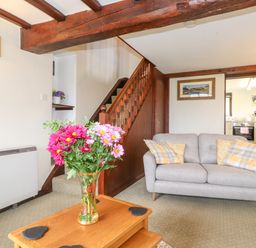 A living room with a gray sofa and a wooden coffee table with flowers near a wooden staircase at Addylea Cottage in Cartmel Fell near Windermere