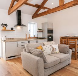 A kitchen with white cabinets wooden countertops and a beige sofa with animal print pillows at Pear Tree Cottage in St Mellion near St Dominick