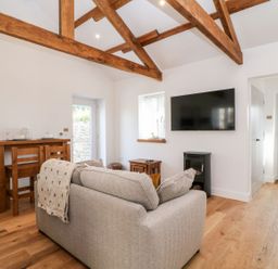 A living room with grey sofa wooden beams wooden floor wall mounted TV and wooden dining table at Pear Tree Cottage in St Mellion near St Dominick