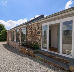The exterior of a stone building with large windows and an open door on a gravel driveway at Old Orchard Barn St Mellion near St Dominick