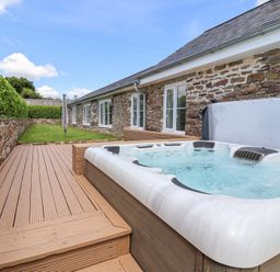 An outdoor deck with a hot tub and a lawn area beside a stone building at Old Orchard Barn St Mellion near St Dominick