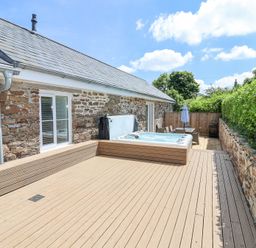 An outdoor deck with a hot tub dining table chairs umbrella and stone wall at Old Orchard Barn St Mellion near St Dominick