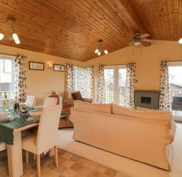 A combined dining and living room with a wooden ceiling and large windows at Lodge 16 in Whitsand Bay near Millbrook