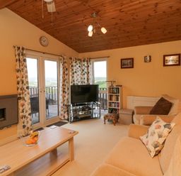 A living room with beige sofas a wooden coffee table and a television near French doors at Lodge 16 in Whitsand Bay near Millbrook