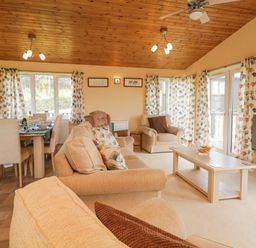 A living room and dining area with beige sofas a coffee table dining table and floral curtains at Lodge 16 Whitsand Bay near Millbrook