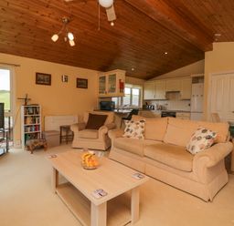 A living room with beige sofas a coffee table with fruit a television and an open kitchen at Lodge 16 Whitsand Bay near Millbrook