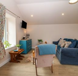A living room with a blue sofa, patterned cushions, small tables, a blue cabinet, and a wall-mounted television at Y Felin in Caernarfon