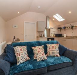 A kitchen and living room area with a blue sofa and patterned cushions at Y Felin in Caernarfon