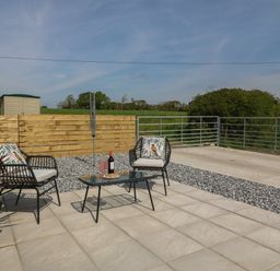 An outdoor patio with two chairs and a glass table with a bottle and glasses at Y Felin in Caernarfon