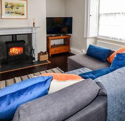 A living room with a fireplace wood burning stove and a grey sofa with blue and orange cushions at Carew House Cottage in St Day