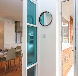 A dining area with table and chairs next to a kitchen and an open door to an outside brick wall at Sandy Toes in Paignton