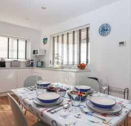 A dining table set with bowls plates glasses and cutlery in a kitchen with white cabinets and windows at Sandy Toes Paignton