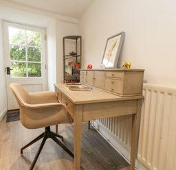 A desk with small drawers and decorative elephants next to a beige chair in a room with a glass door at Half Pint Cottage in Beaminster