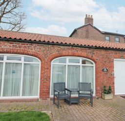 Exterior of a brick cottage with two large arched windows a white door two outdoor chairs and plants at Fulmar Cottage in Flamborough