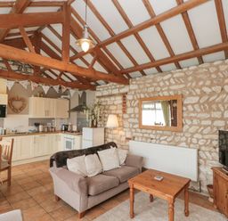 A living area with kitchen cabinets dining table sofa coffee table television and stone walls at Fulmar Cottage in Flamborough