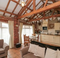 An open plan living area with beige sofas a small dining table wooden chairs and a kitchen with cream cupboards under exposed wooden beams at Fulmar Cottage in Flamborough