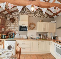 A kitchen with cream cabinets wooden countertops a washing machine a dining table and chairs stone and brick walls at Fulmar Cottage in Flamborough
