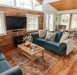 A living room with two blue sofas a coffee table with flowers and snacks a television on a wooden wall and a dining table with chairs at The Bird House in Cenarth