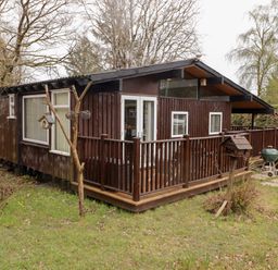 A wooden house with a small fenced porch surrounded by grass and trees at The Bird House in Cenarth