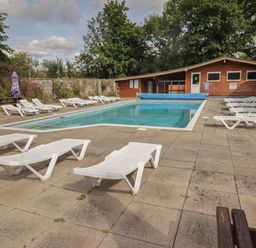 An outdoor swimming pool with white lounge chairs around and wooden buildings in the background at The Bird House in Cenarth