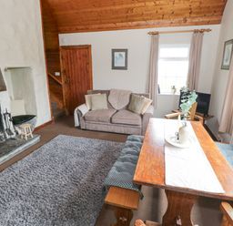 A living room with a fireplace a sofa wooden dining table with benches and windows at Bofin in Oughterard County Galway