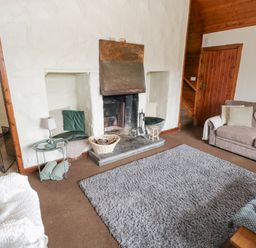 A living room with a fireplace cushions on built in seats sofas and a gray rug at Bofin in Oughterard County Galway