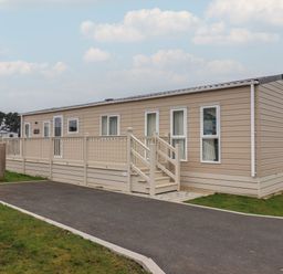 A beige mobile home with a small staircase and a railing on the side at Whispering Willows in Cayton Bay